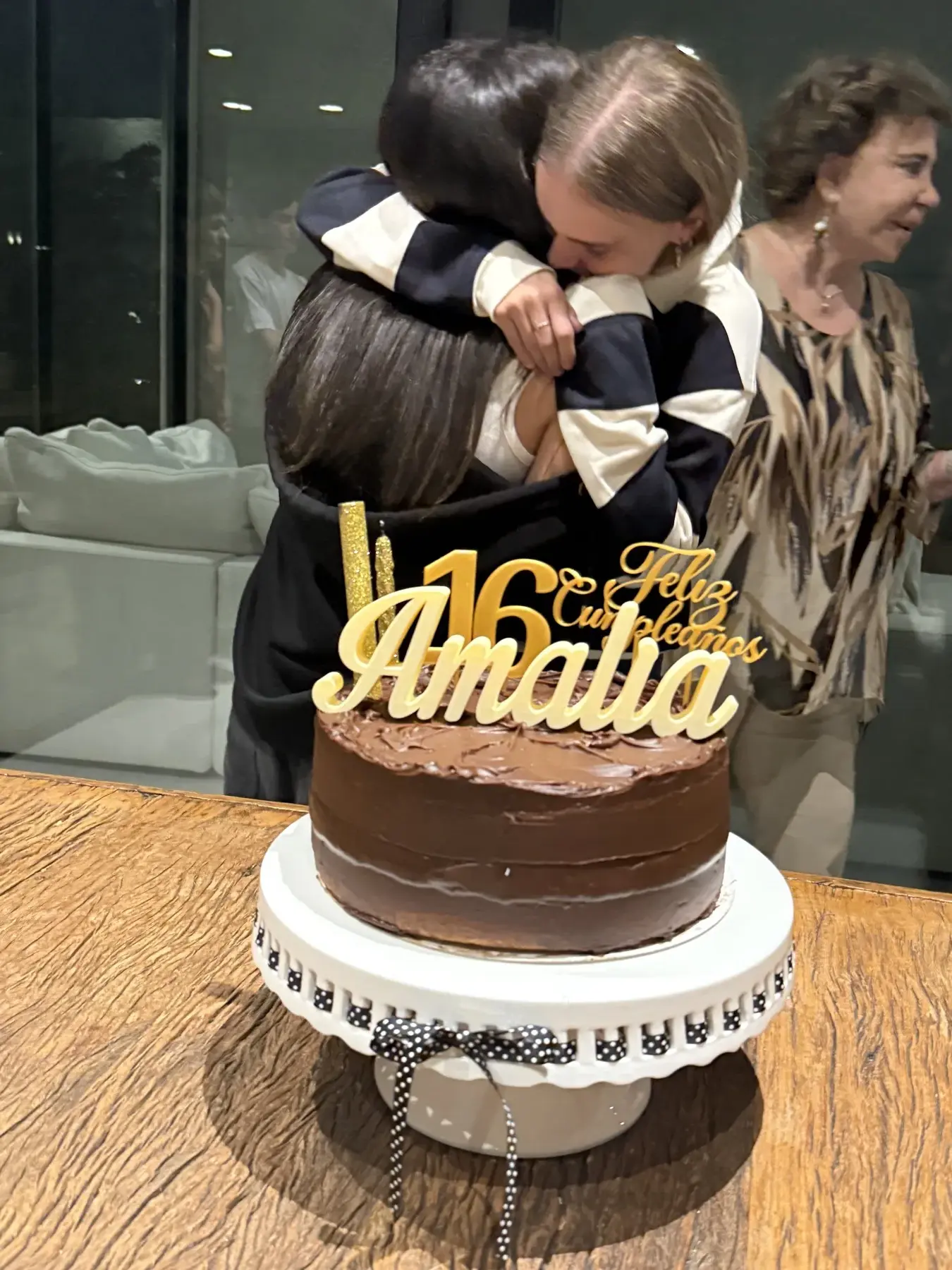 Amalia abrazando a su mamá con el cake topper Feliz Cumple 16 Amalia dorado sobre la torta de chocolate