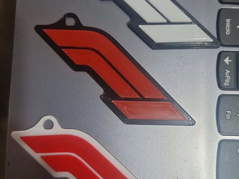 3 llaveros 3D del logo de Fórmula 1 que recibió Martina: blanco con borde azul, rojo con borde azul, y rojo con borde blanco